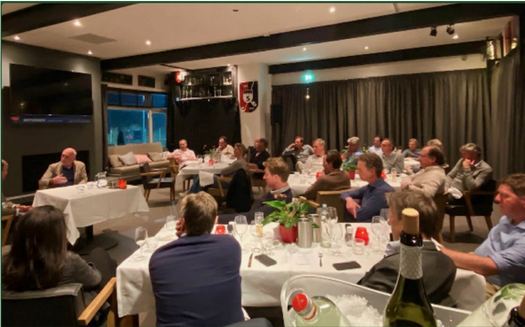 Lange diner-tafel bij kaarslicht, gasten in gesprek tussen de gangen door